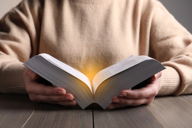 Photo of Woman reading Bible at wooden table, closeup