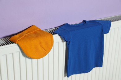 Photo of Bright hat and t-shirt on heating radiator near violet wall