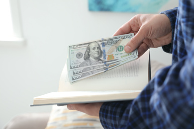 Man hiding dollar banknotes in book indoors, closeup. Money savings