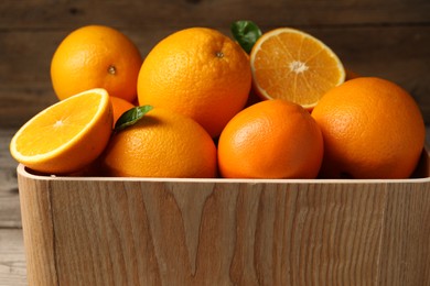 Many whole and cut ripe oranges on wooden table, closeup