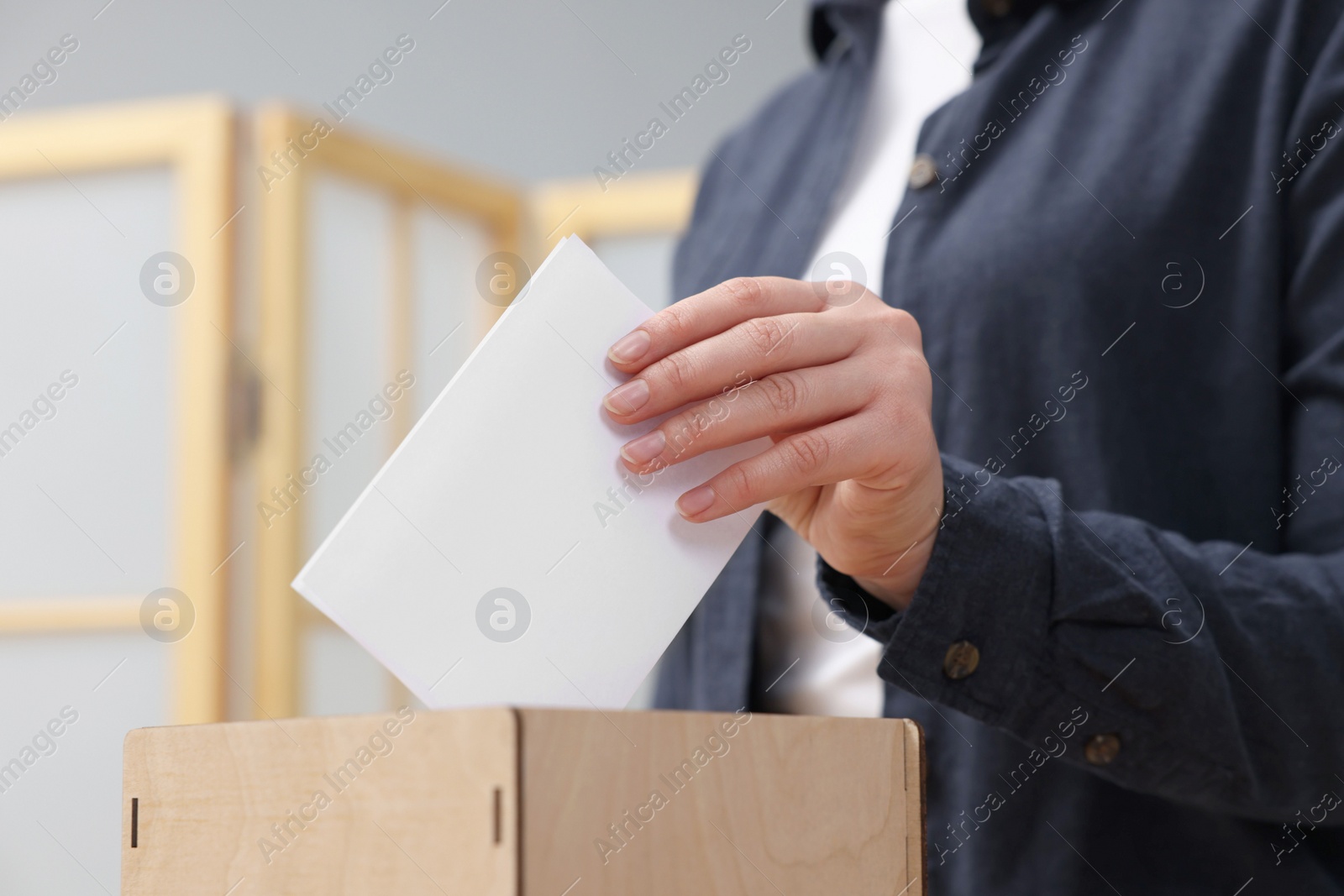 Photo of Woman putting her vote into ballot box on blurred background, closeup