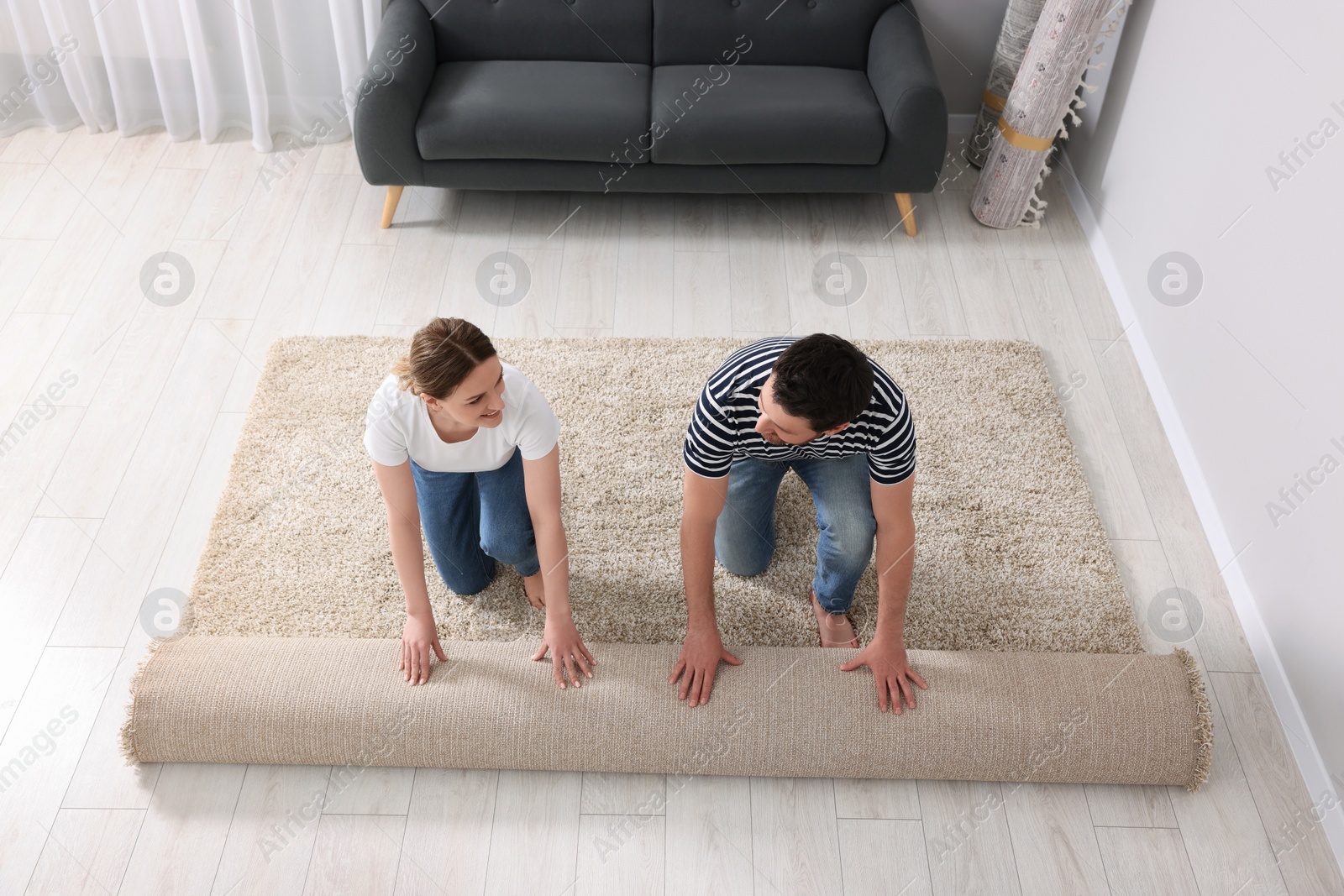 Photo of Smiling couple unrolling carpet on floor in room