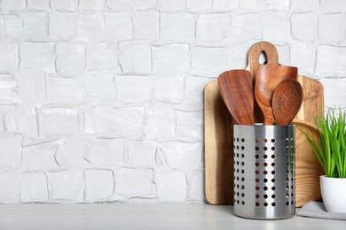 Photo of Set of wooden kitchen utensils, board and houseplant on table near white wall. Space for text