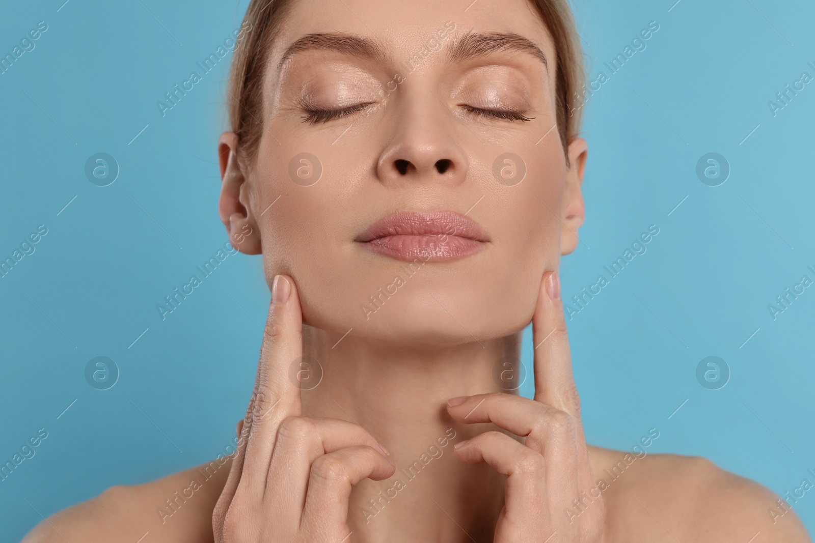 Photo of Woman massaging her face on turquoise background