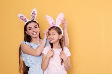 Photo of Mother and daughter in Easter bunny ears headbands on color background, space for text