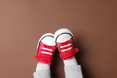 Photo of Little child in stylish red gumshoes on brown background, top view