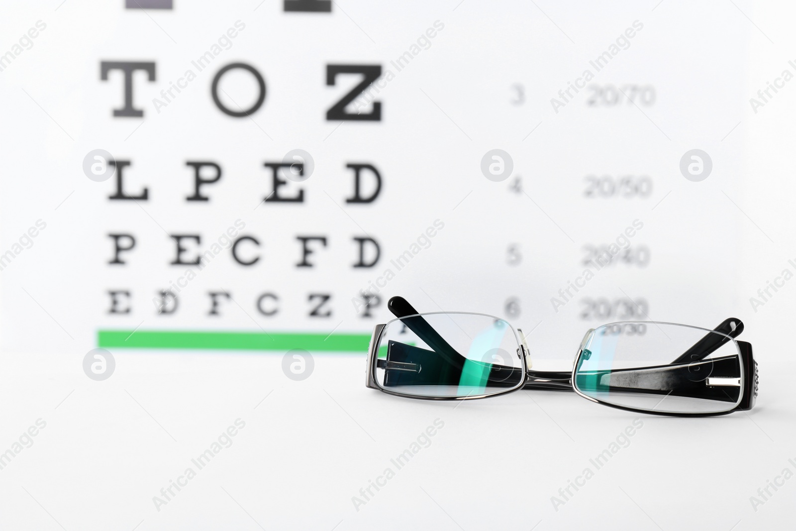Glasses with corrective lenses on table against eye chart Photo of Glasses with corrective lenses on table against eye chart
