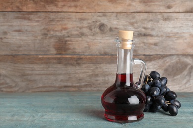 Glass jug with wine vinegar and fresh grapes on wooden table. Space for text