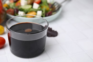 Photo of Vinegar in glass on white tiled table, closeup. Space for text