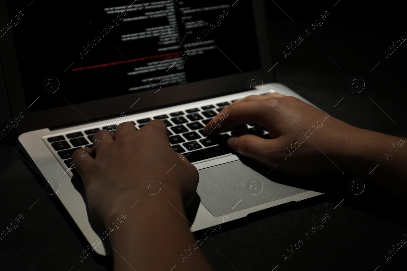 Photo of Hacker working with laptop in darkness, closeup of hands. Cyber crime