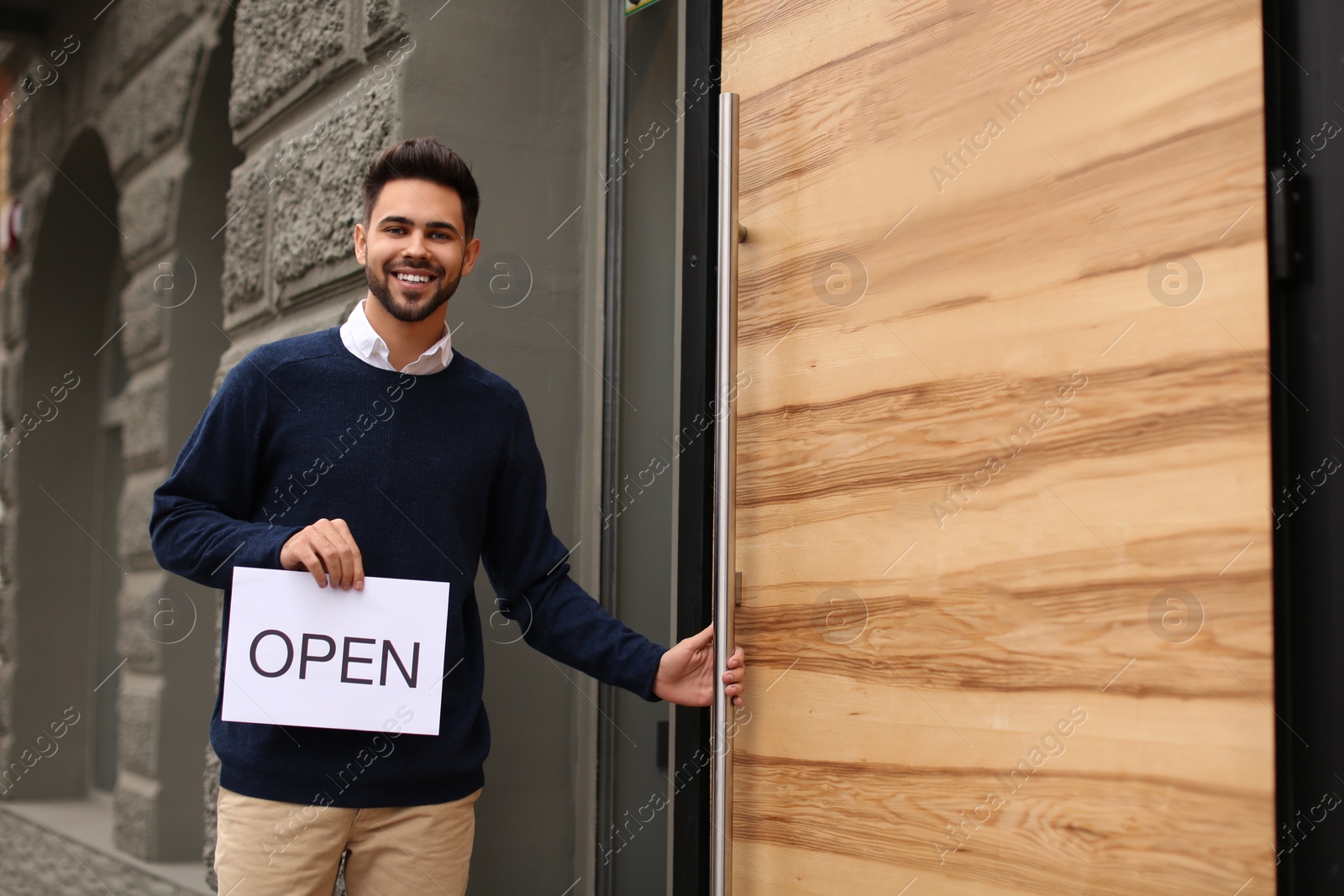 Photo of Young male business owner holding OPEN sign near his cafe