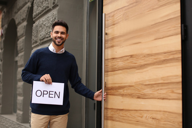 Photo of Young male business owner holding OPEN sign near his cafe