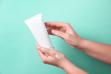 Photo of Woman with tube of hand cream on turquoise background, closeup