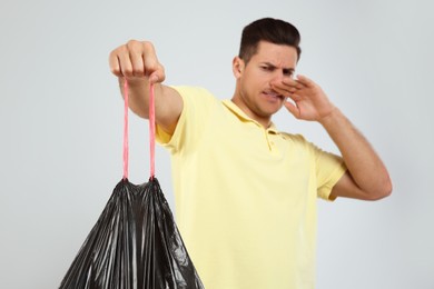 Photo of Man holding full garbage bag against light background, focus on hand