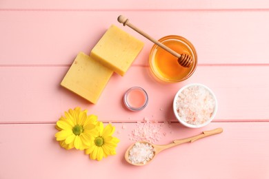 Photo of Natural beeswax, lip balm, honey, sea salt and flowers on pink wooden table, flat lay