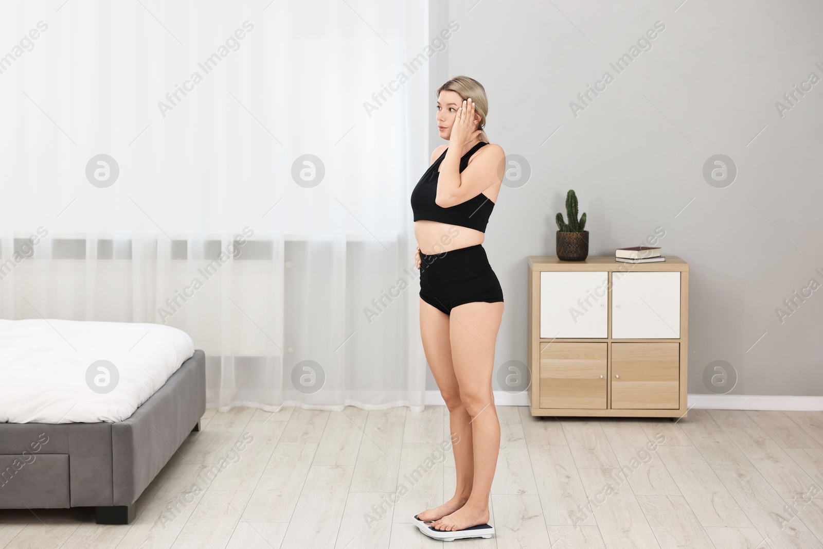 Photo of Surprised woman standing on floor scales at home