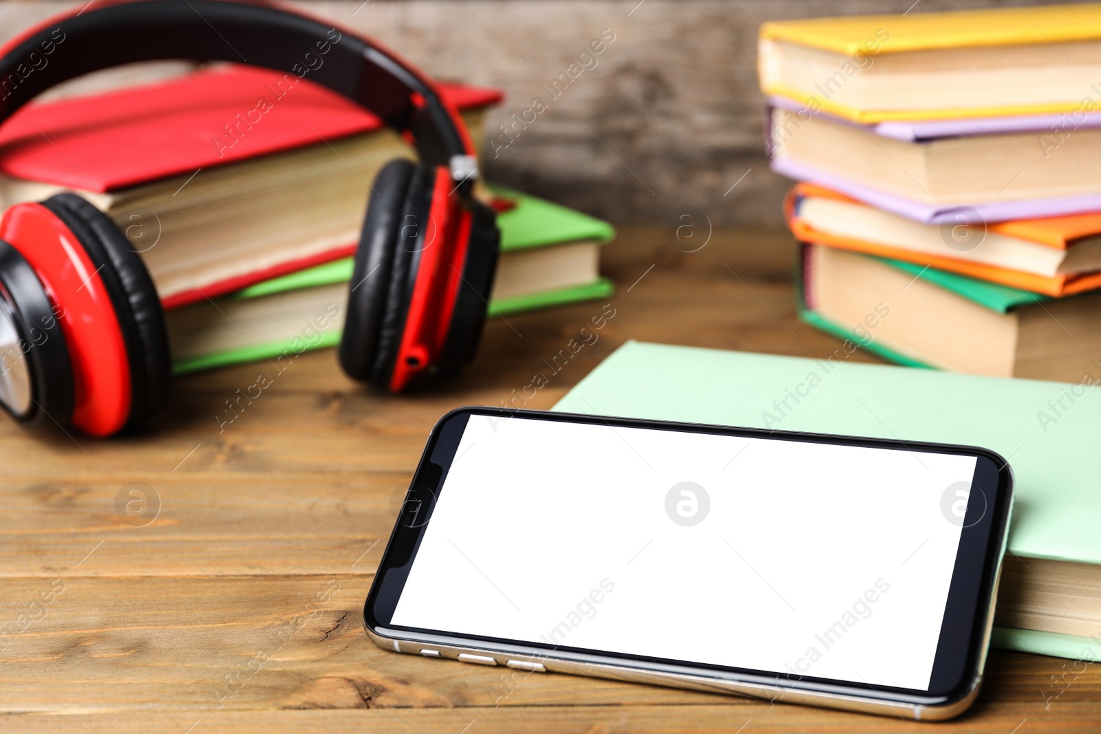 Photo of Modern smartphone with blank screen and books on wooden table, closeup. Space for design