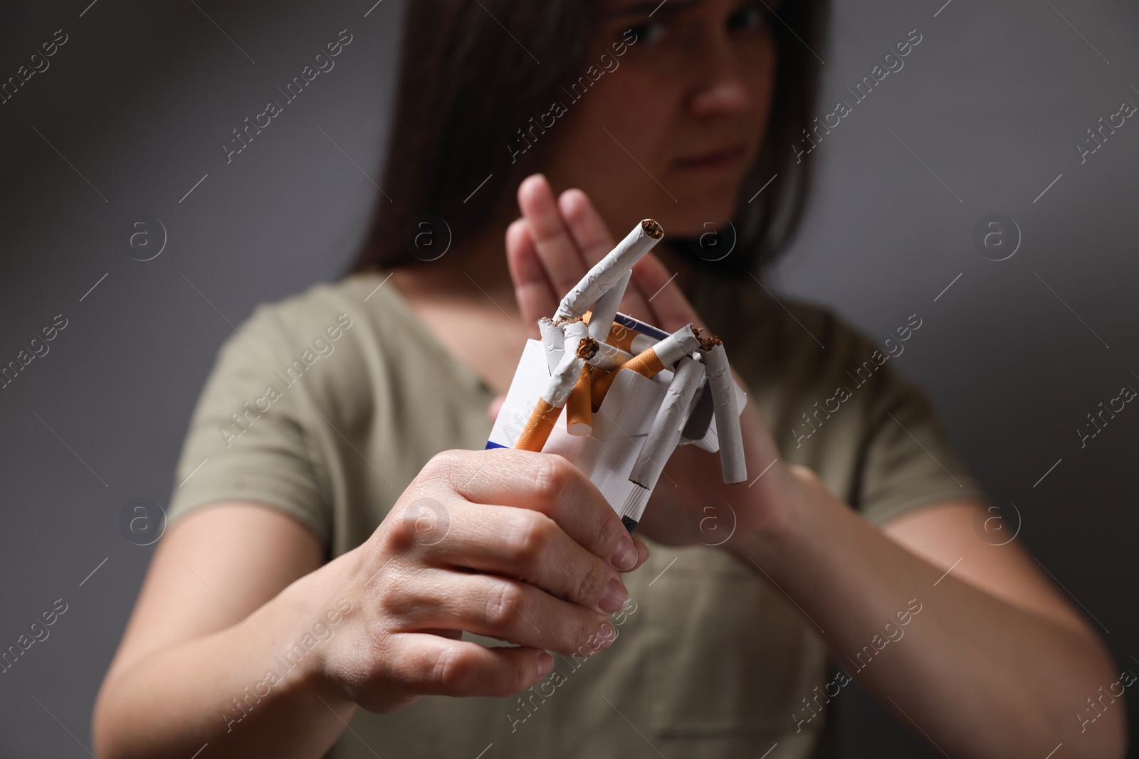 Photo of Stop smoking. Woman holding pack with broken cigarettes on grey background, selective focus