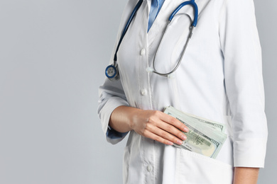 Doctor putting bribe into pocket on grey background, closeup. Corruption in medicine