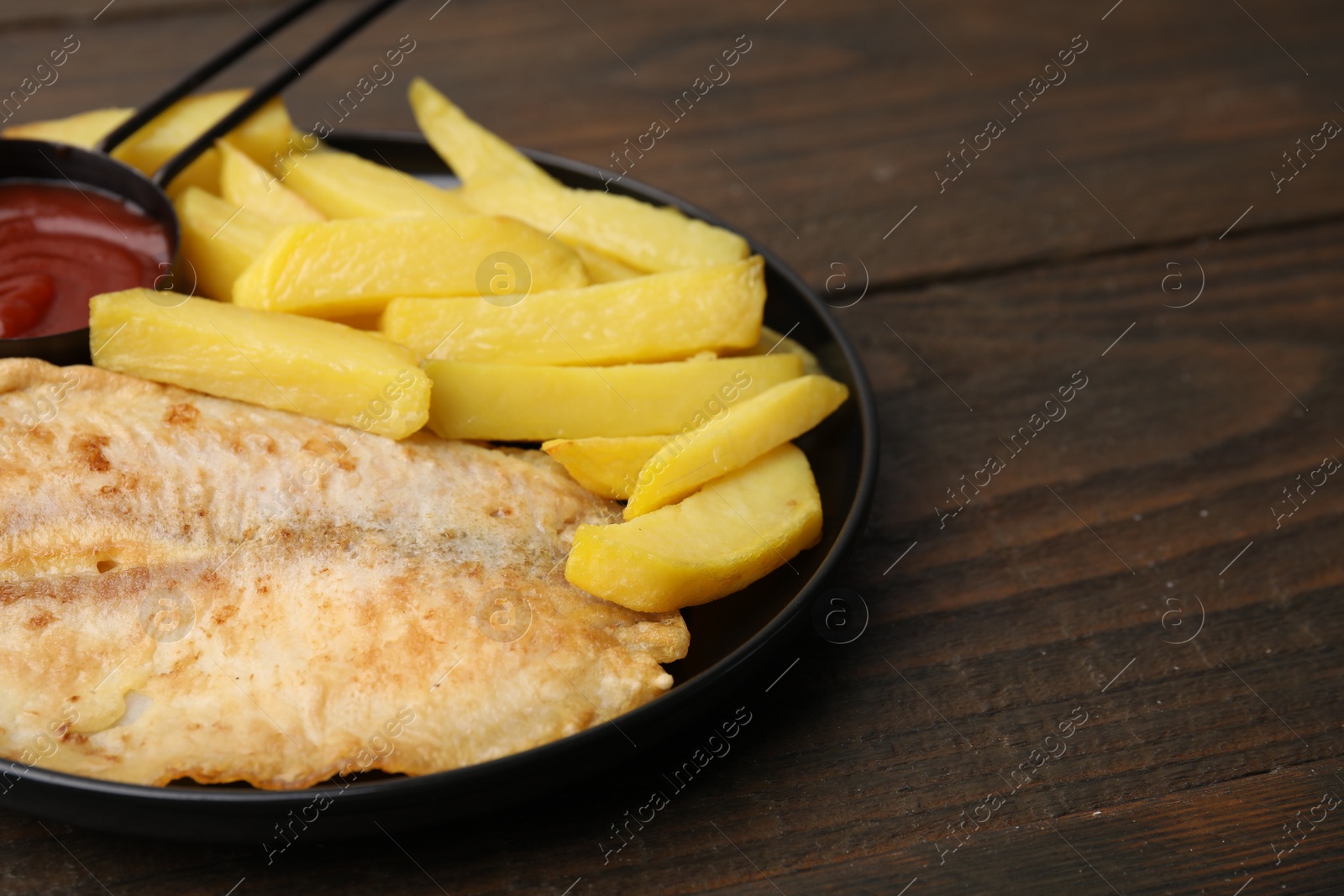 Photo of Delicious fish and chips with ketchup on wooden table, closeup