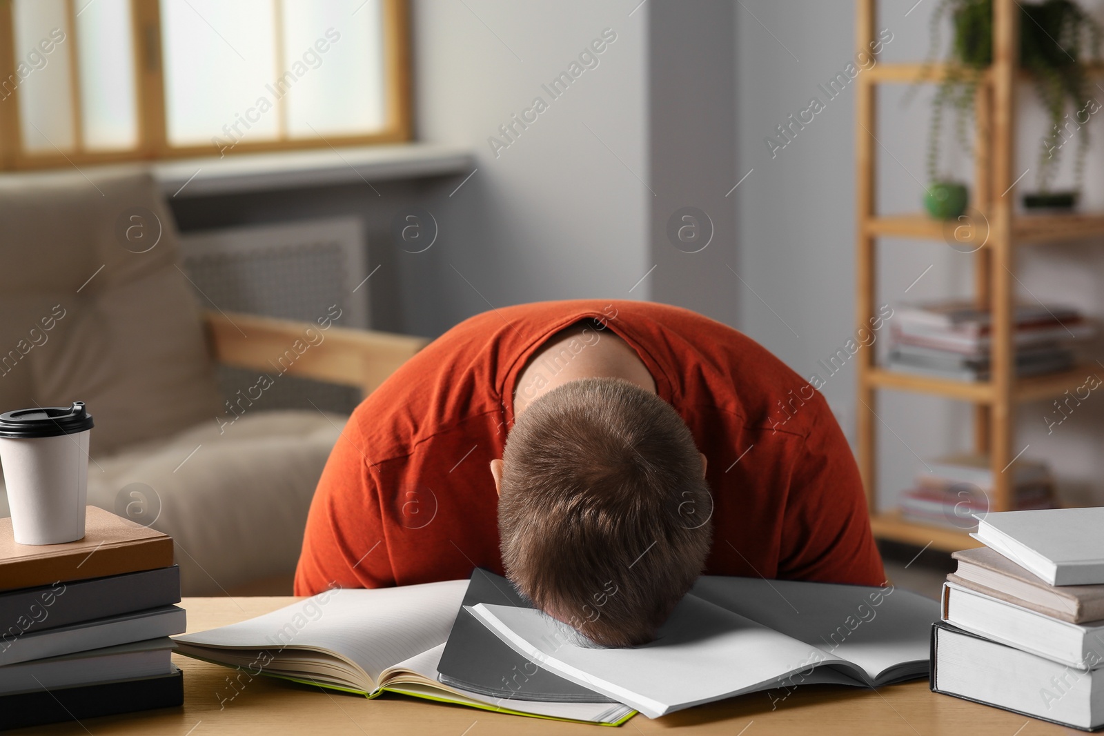 Photo of Tired man sleeping near books at wooden table indoors