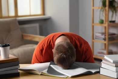 Tired man sleeping near books at wooden table indoors