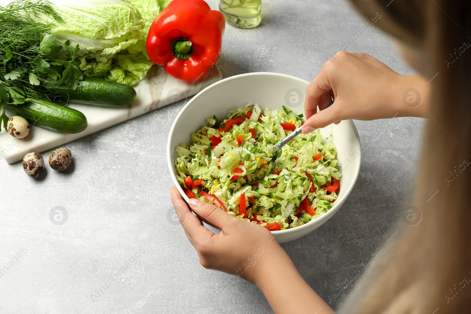 Photo of Woman making tasty salad with Chinese cabbage at light grey table, closeup