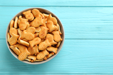 Delicious goldfish crackers in bowl on light blue wooden table, top view. Space for text