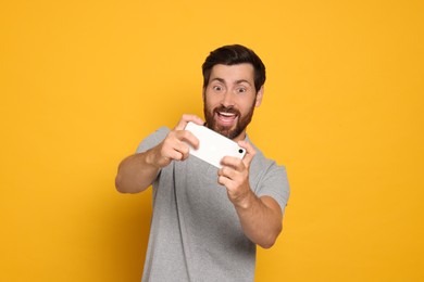 Emotional man playing game on smartphone against yellow background
