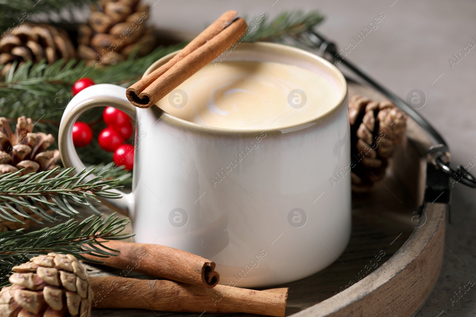 Photo of Tasty eggnog with cinnamon sticks on grey table, closeup