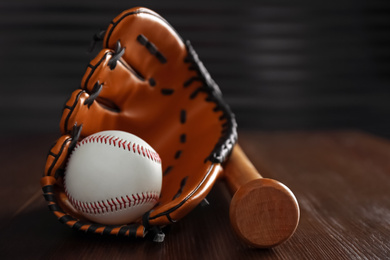 Photo of Leather baseball ball, bat and glove on wooden table, closeup