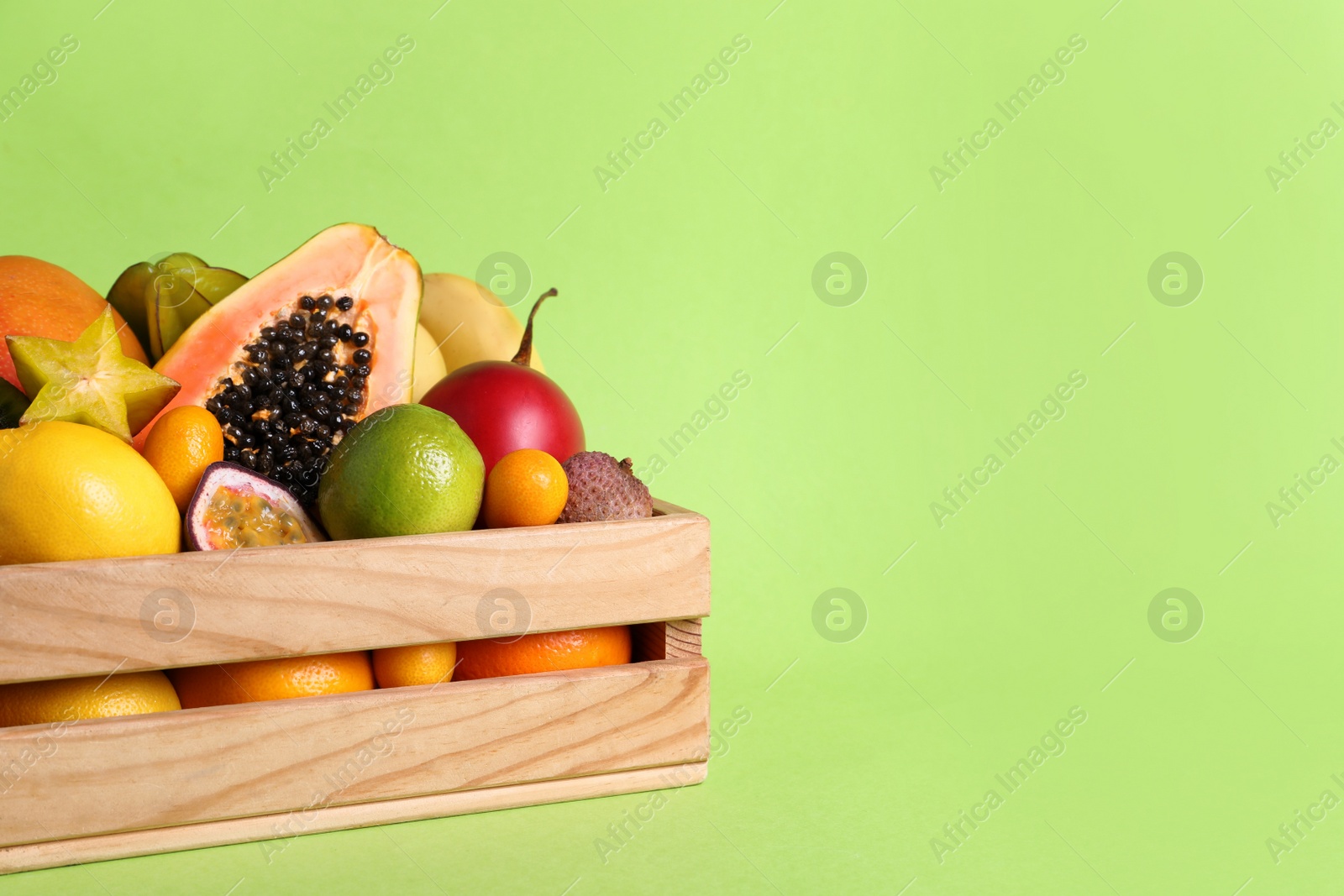 Photo of Different tropical fruits in wooden box on green background. Space for text