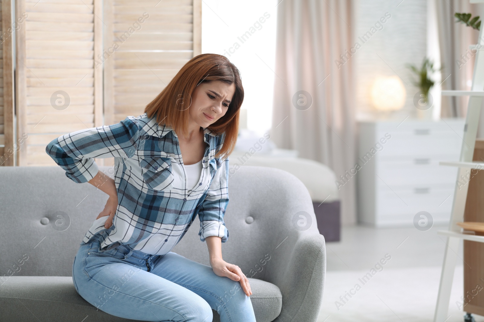 Photo of Young woman suffering from back pain at home