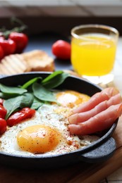 Delicious fried eggs with spinach, tomatoes and ham served on table