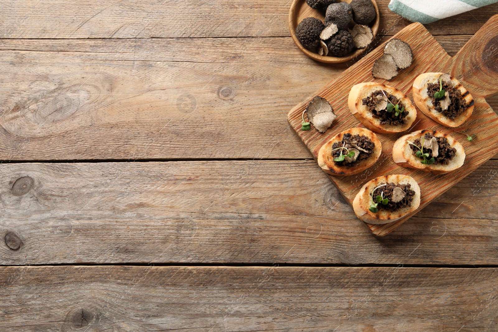 Photo of Delicious bruschettas with truffle sauce and microgreens on wooden table, flat lay. Space for text