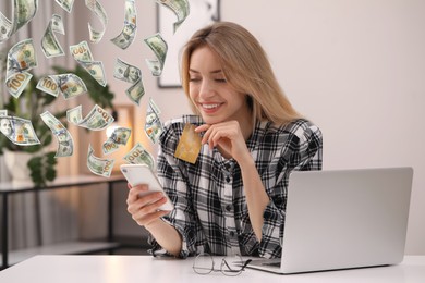 Image of Online payment. Woman with credit card buying something using mobile phone at home. Dollar banknotes flying out of gadget as process of money transaction