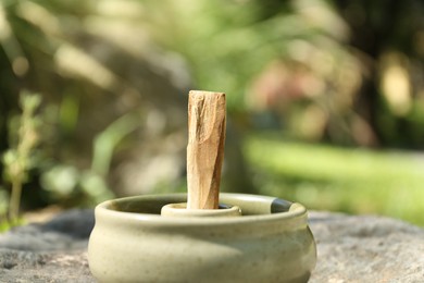 Palo santo stick in holder on stone outdoors, closeup