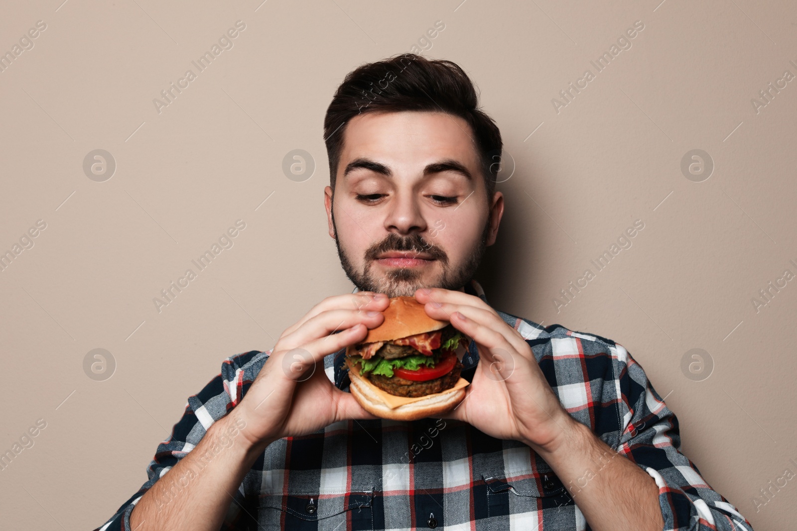 Photo of Handsome man eating tasty burger on color background