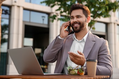 Photo of Happy businessman talking on smartphone during lunch at wooden table outdoors