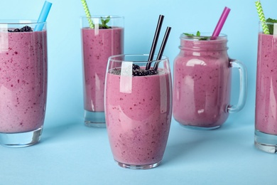 Delicious blackberry smoothie in different glassware on light blue background