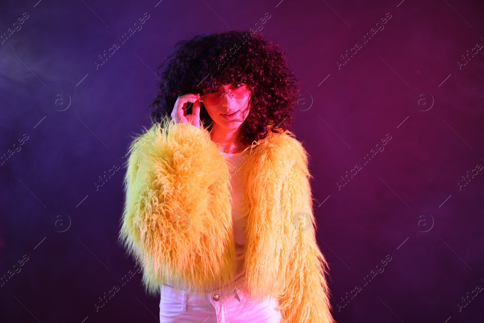 Photo of Beautiful young woman in yellow fur coat and sunglasses on color background in neon lights