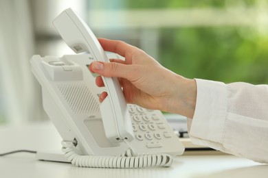 Photo of Assistant taking telephone handset at white table, closeup