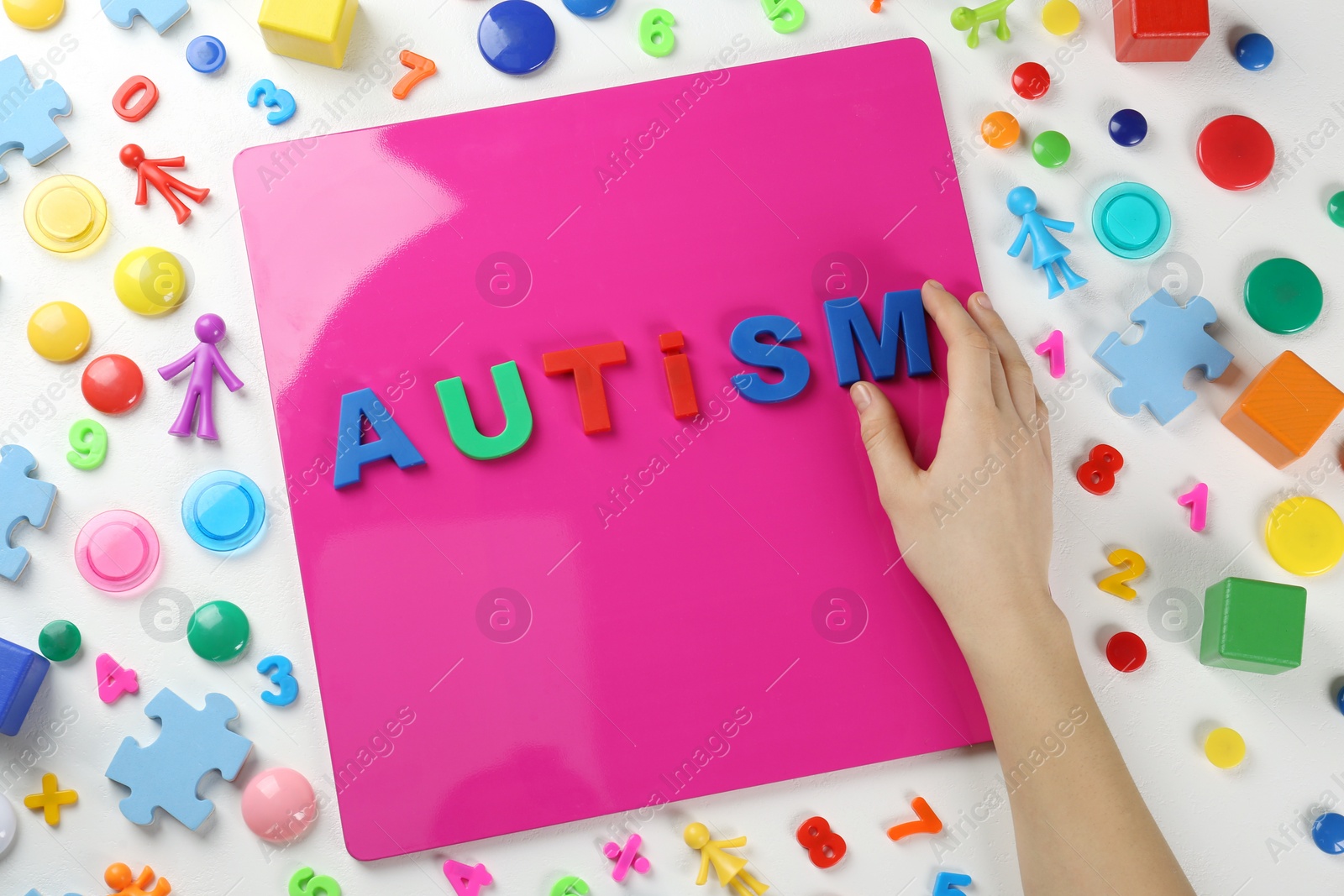 Photo of MYKOLAIV, UKRAINE - DECEMBER 30, 2021: Woman making word Autism on magnetic board at table with toys