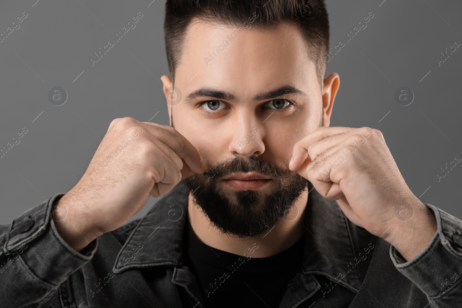 Photo of Young man touching mustache on grey background