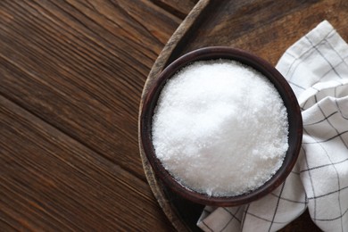 Photo of Organic salt in bowl on wooden table, top view. Space for text