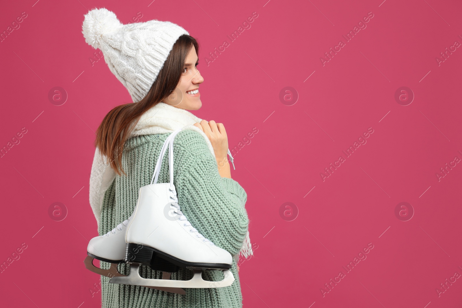 Photo of Happy woman with ice skates on pink background. Space for text
