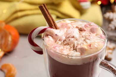 Delicious marshmallow drink with cinnamon and candy cane in cup on blurred background, closeup