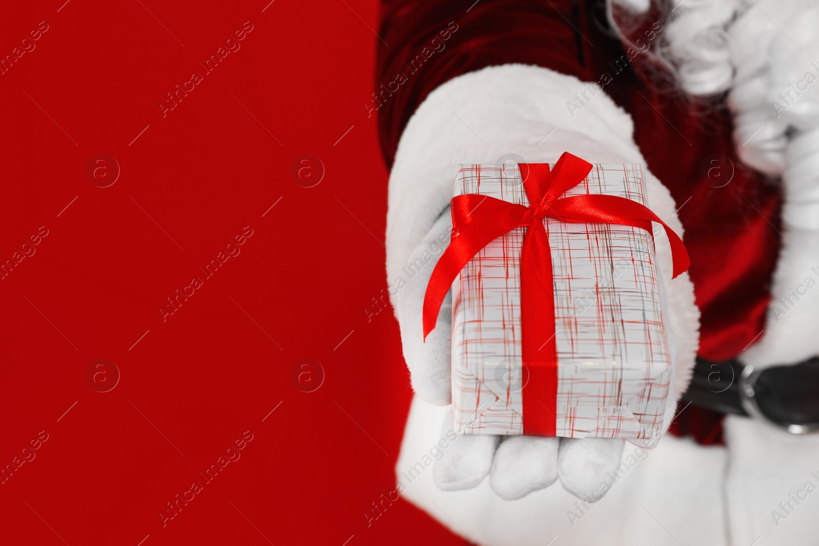 Photo of Santa Claus holding Christmas gift on red background, closeup. Space for text