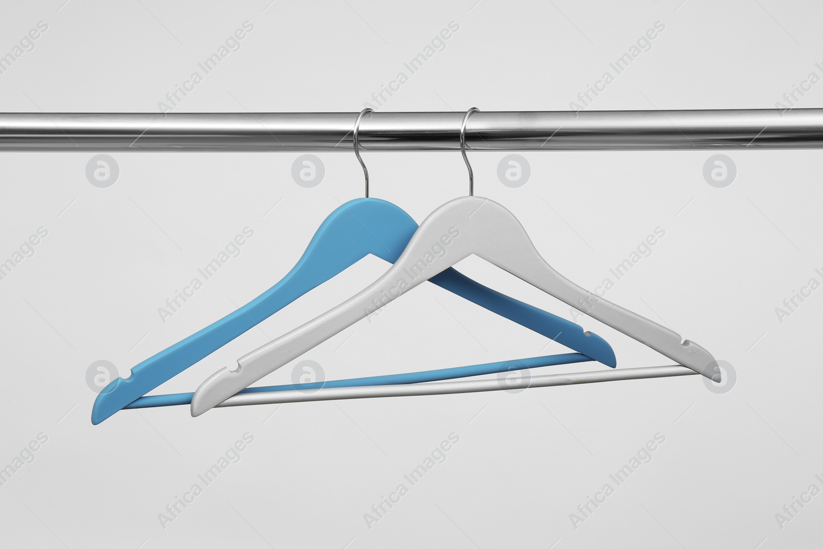 Photo of Empty clothes hangers on metal rail against light background