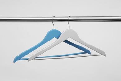 Photo of Empty clothes hangers on metal rail against light background